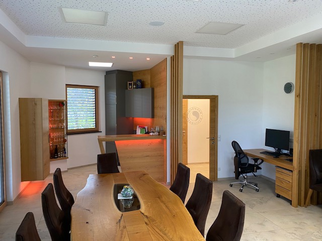 Eleganter Besprechungstisch mit hochwertigen Sesseln, modernem Arbeitsplatz und einer stilvollen Küche im Hintergrund.